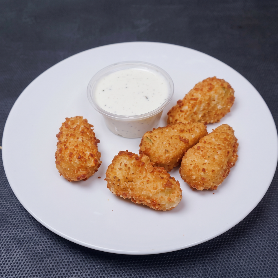 Golden-brown breaded cheese sticks arranged on a white plate with a cup of creamy dipping sauce.
